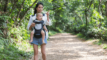 Mom carrying baby in ergonomic baby carrier while walking on a forest path, highlighting baby carrier ergonomics.