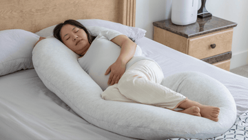 Pregnant woman sleeping with a large U-shaped body pillow on a bed for maternity support