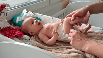 Parent changing baby diaper on changing table, baby lying on towel next to plush toy and wipes.
