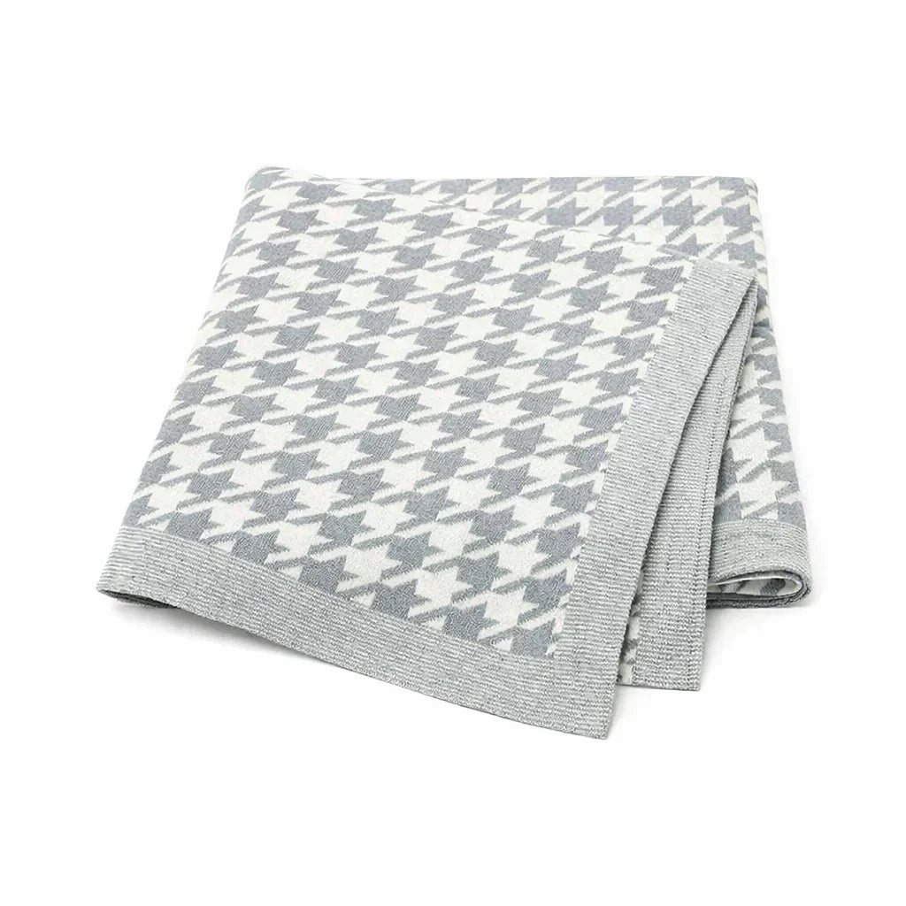Folded grey and white houndstooth knit blanket with a soft border on a white background