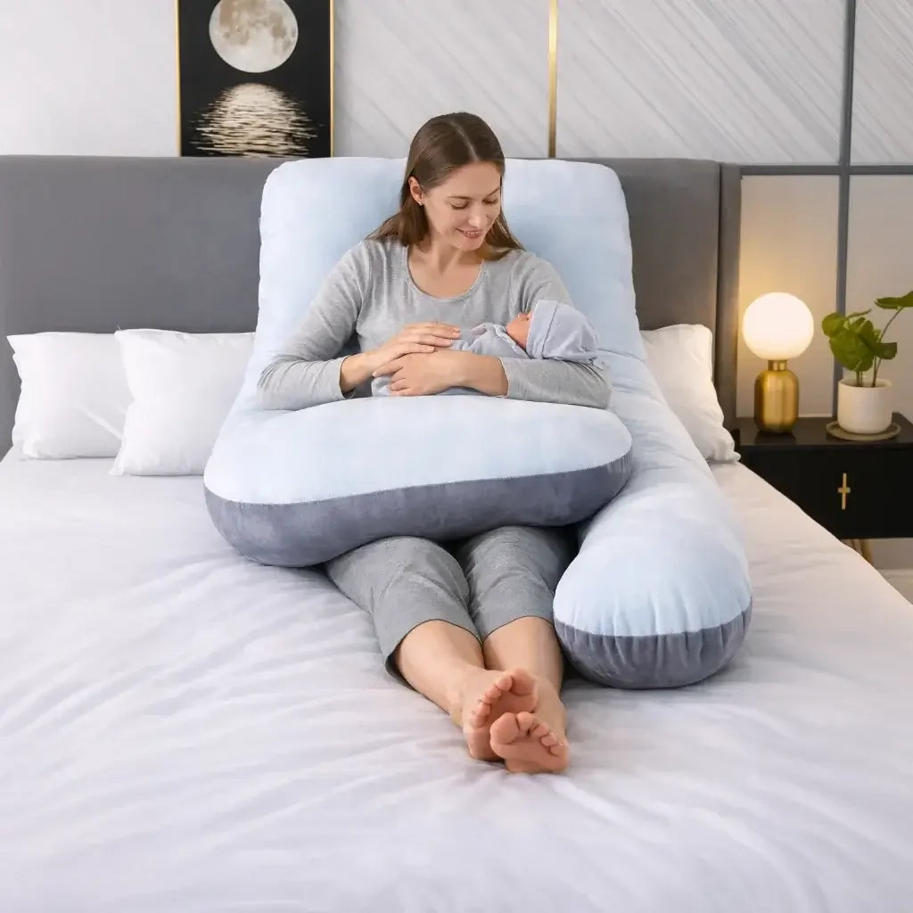 Woman using a large U-shaped pregnancy pillow while nursing a baby on a bed