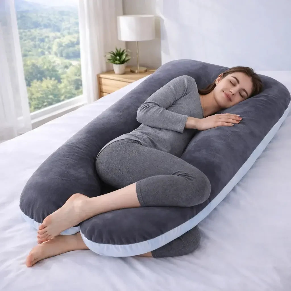 Woman sleeping comfortably on large grey-blue fleece pregnancy pillow on bed.