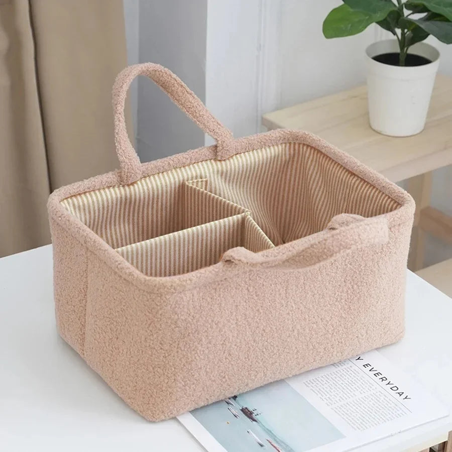 Beige plush storage basket with handles and striped interior dividers on a table