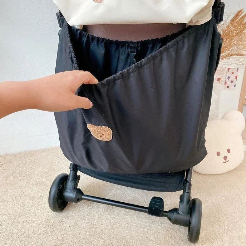 Reusable Stroller Pouch - Hand reaching into black stroller storage pocket with bear patch, indoor setting