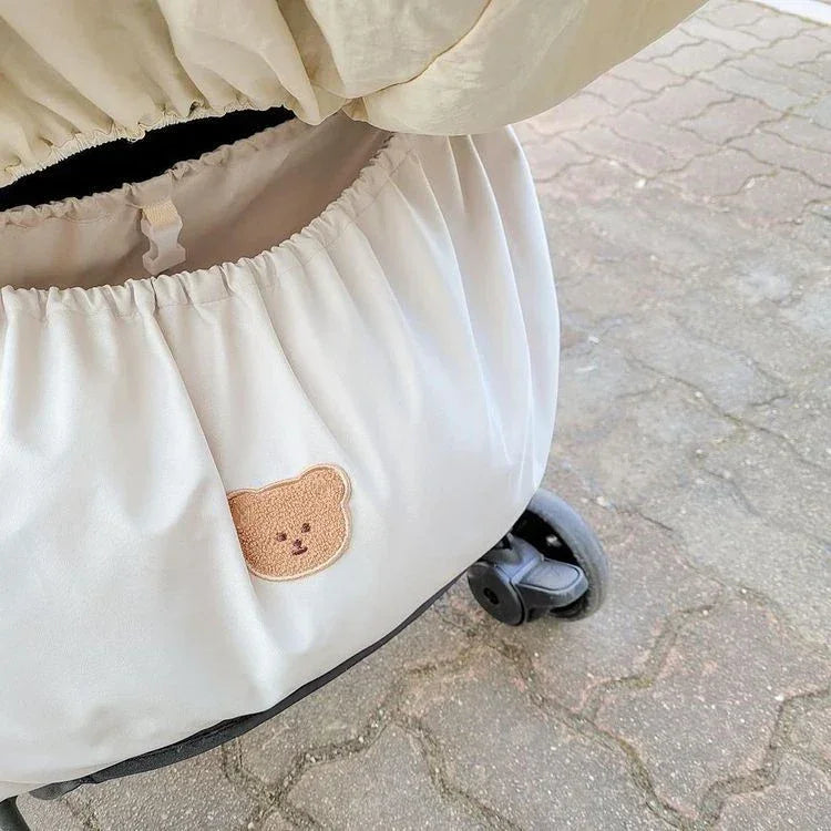 Reusable Stroller Pouch - Beige stroller cover with bear face patch on stroller, outdoor pavement background
