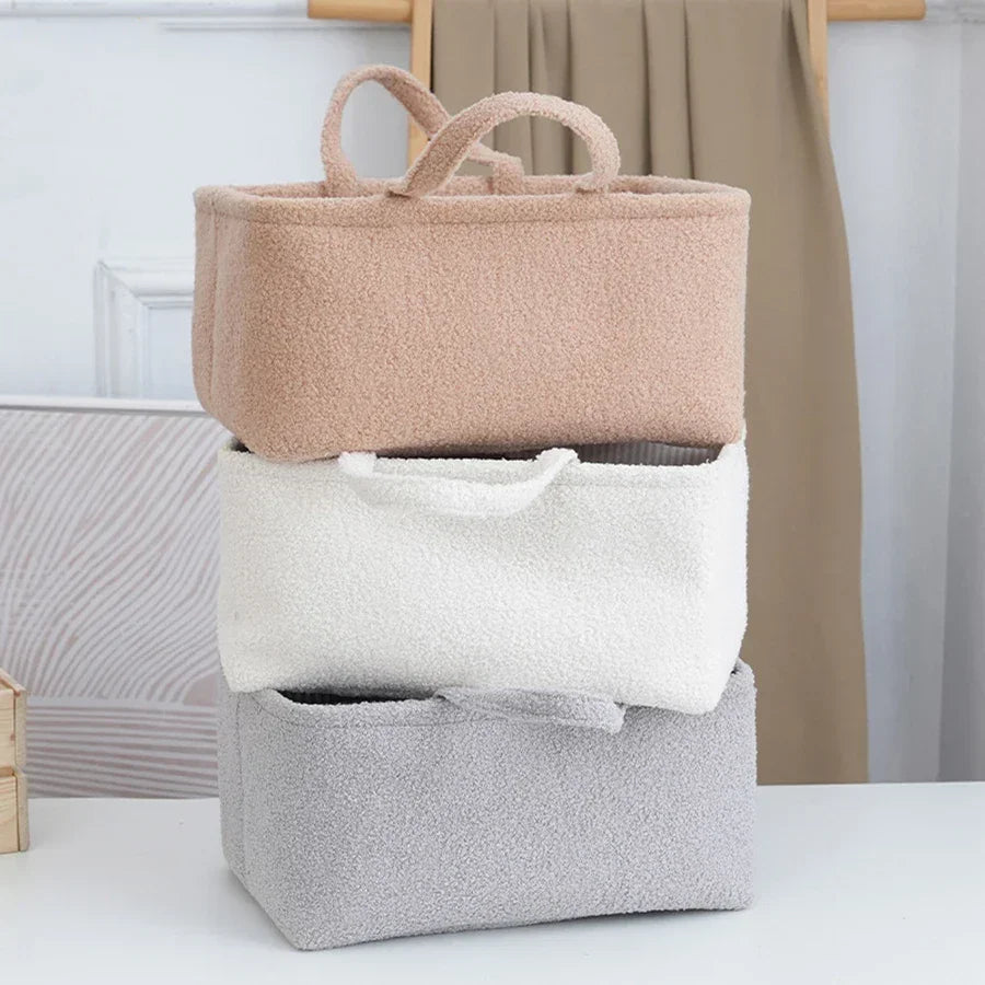 Stack of three soft textured fabric storage baskets in beige, white, and gray on a white table