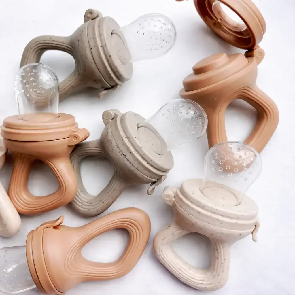 Assorted silicone baby fruit feeders with handles in beige and tan on white background