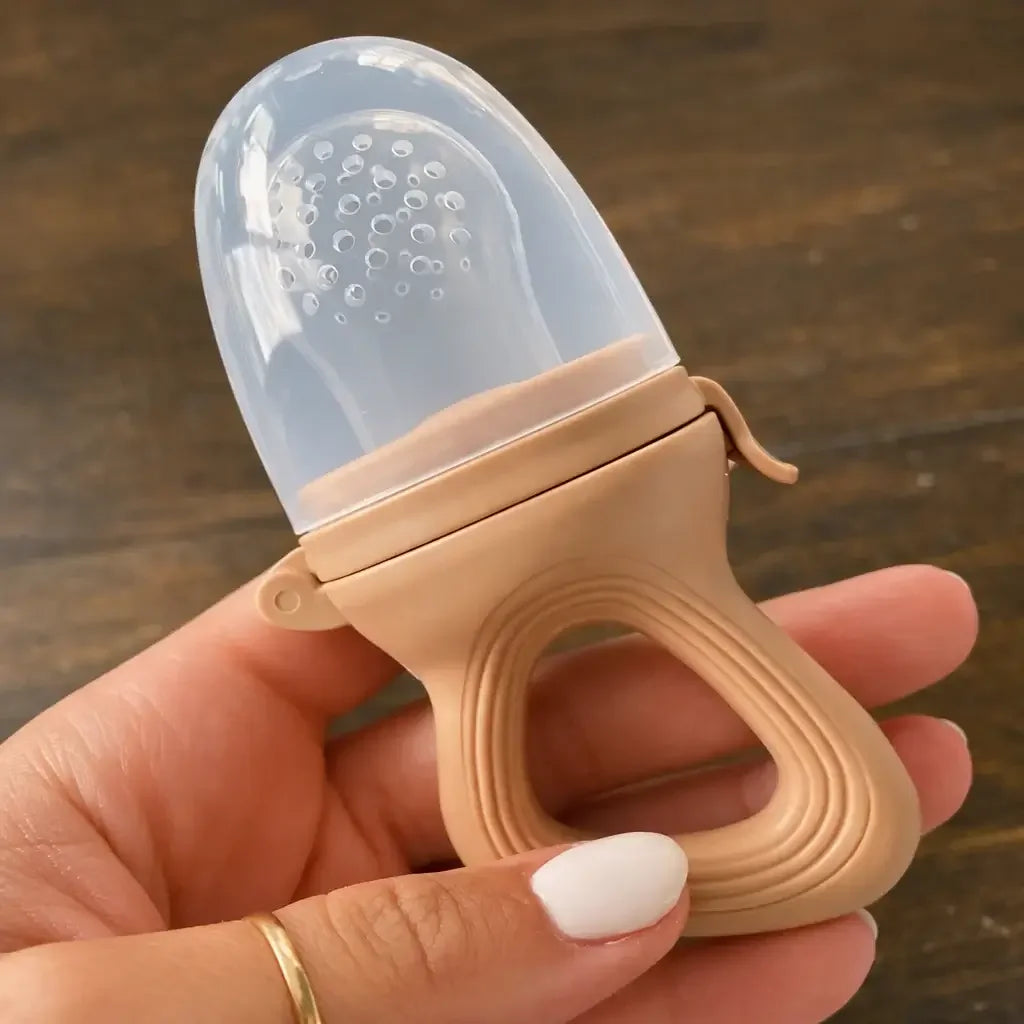 Hand holding a silicone baby fruit feeder with textured handle and clear cap