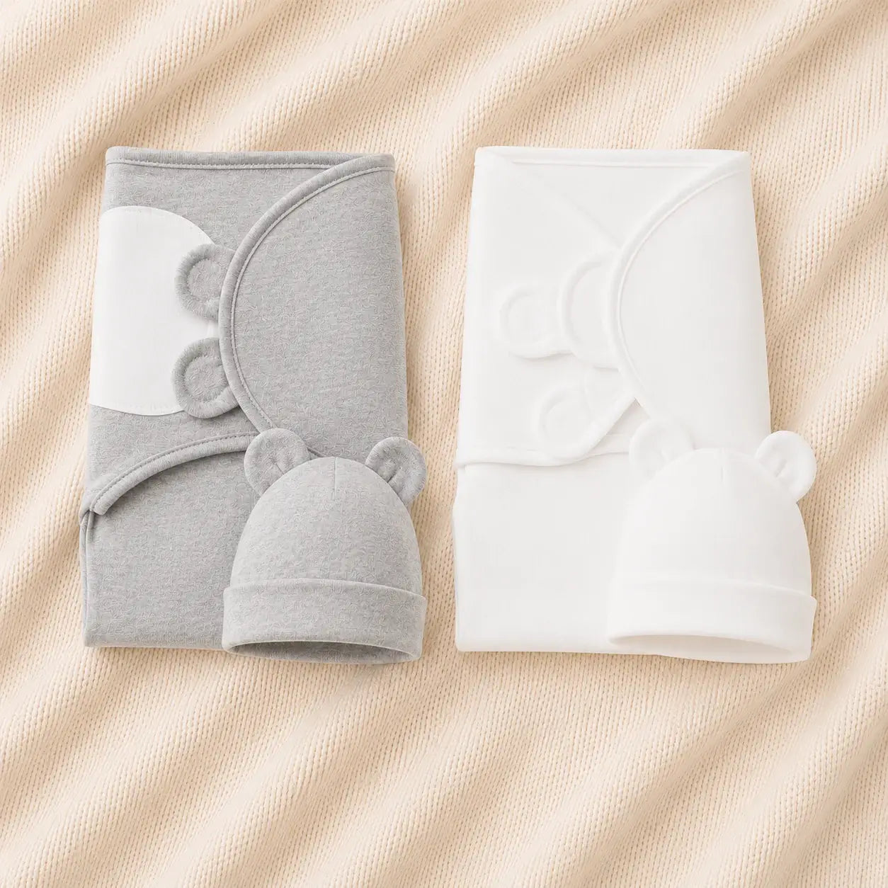 Two adorable newborn adjustable swaddle sets in gray and white with matching bear-themed hats on a soft textured background.