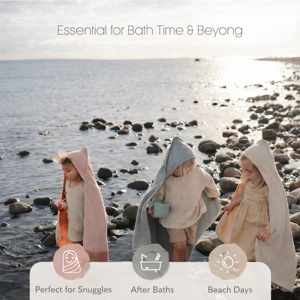 Baby Hooded Towel - Three children in hooded bath towels by a rocky beach, ideal for bath time and beach days.