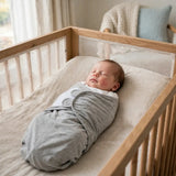 Newborn sleeping peacefully in an adjustable cotton swaddle in a crib.