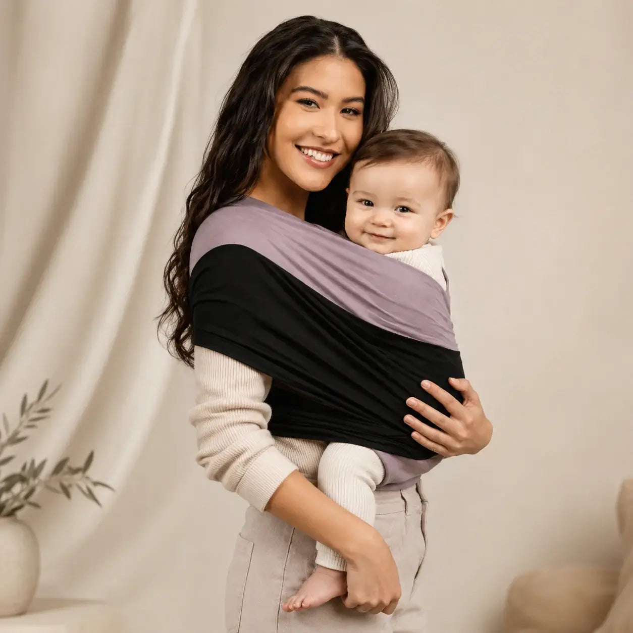 Smiling woman holds baby securely in a baby wrap carrier, showcasing comfort and bonding.